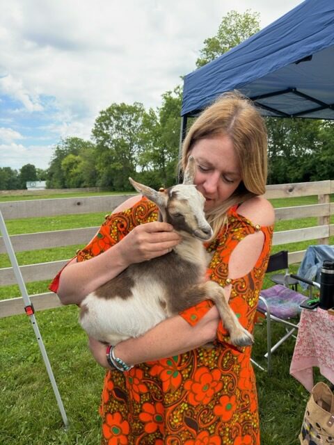 Woman cuddling baby goat in grassy field