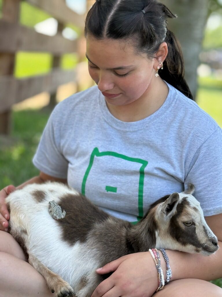 Young woman cradling baby goat outdoors
