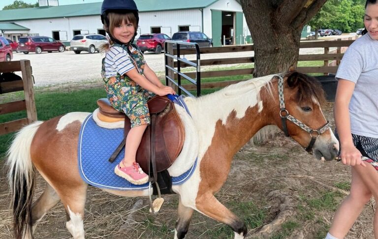 Young girl riding pony at farm