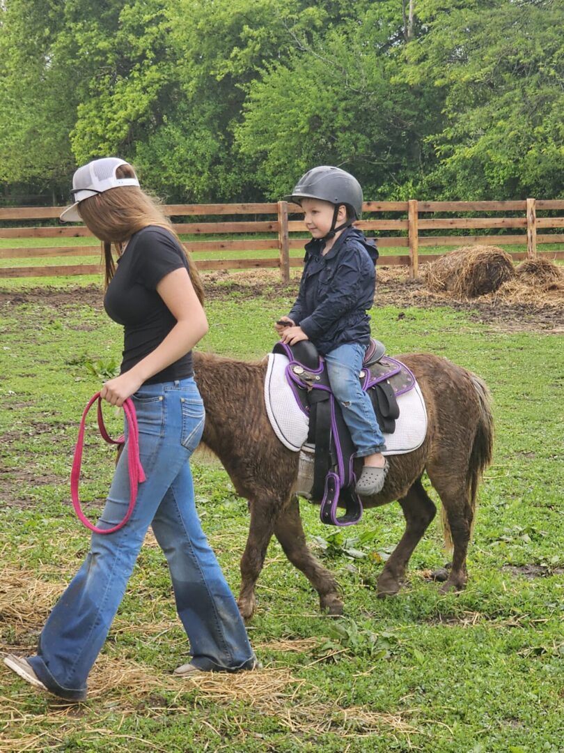 Child wearing helmet riding pony led by woman